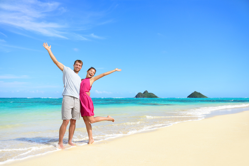 Beach vacation happy carefree couple arms raised. Winning couple with arms up showing happiness and fun on beach with pristine turquoise water on Lanikai beach, Oahu, Hawaii, USA with Mokulua Islands.
